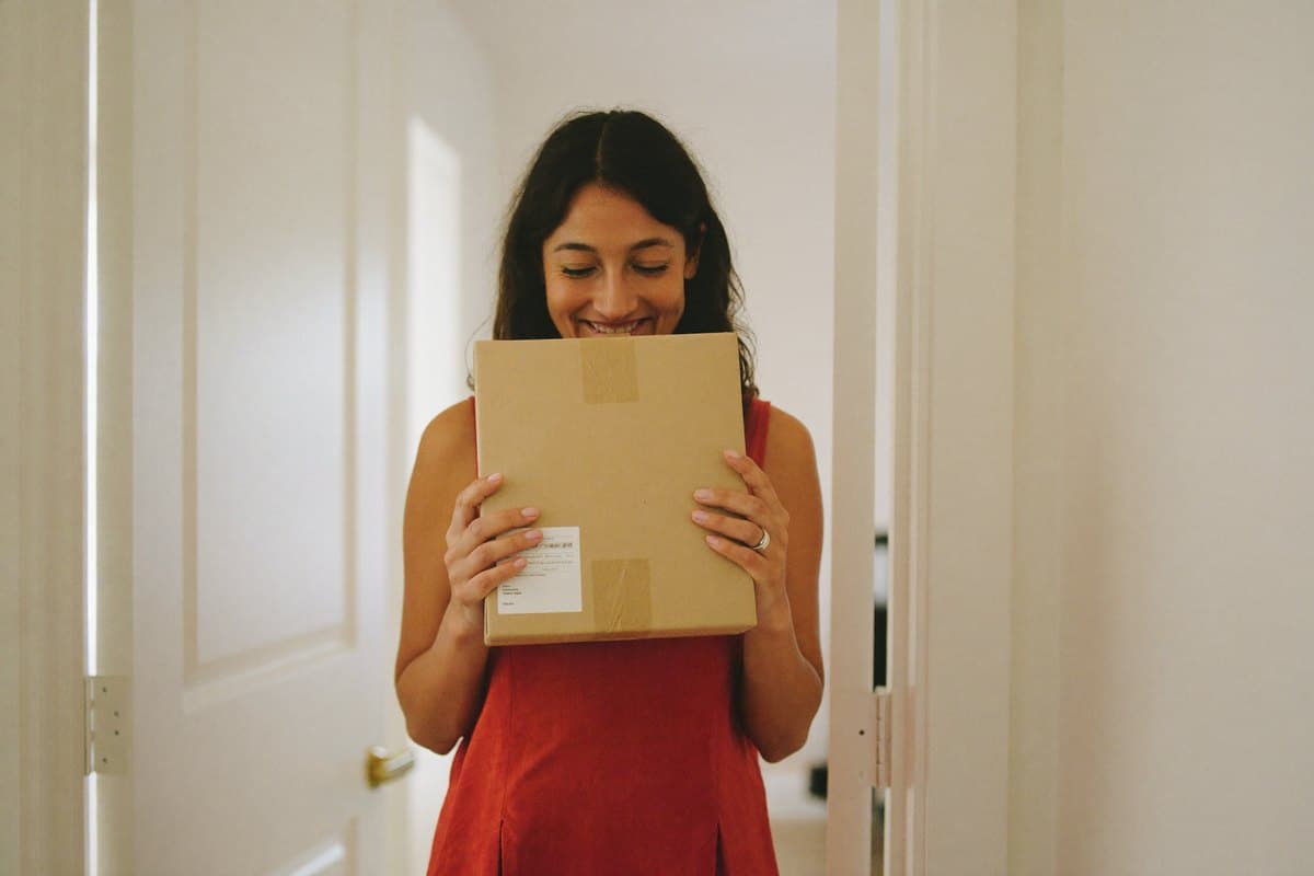 Woman smiling as she receives a small plain parcel at her front door