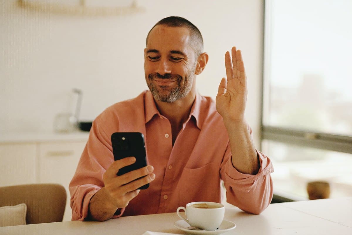 Man sitting relaxed at a bright kitchen table, looking content at his phone