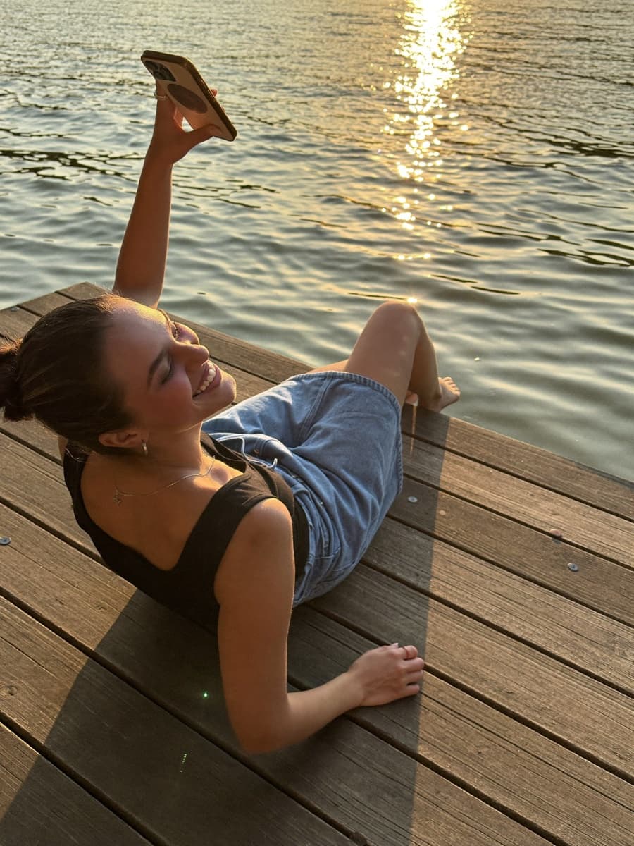 Young woman relaxing on a lake dock, smiling at her phone